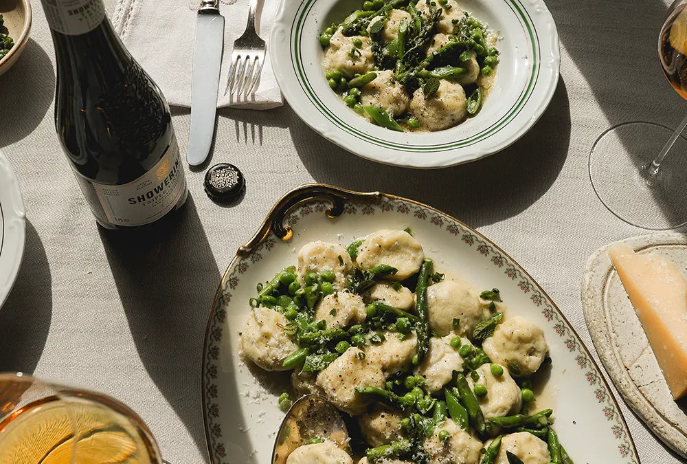 Plate of gnudi with fresh asparagus and peas alongside cider